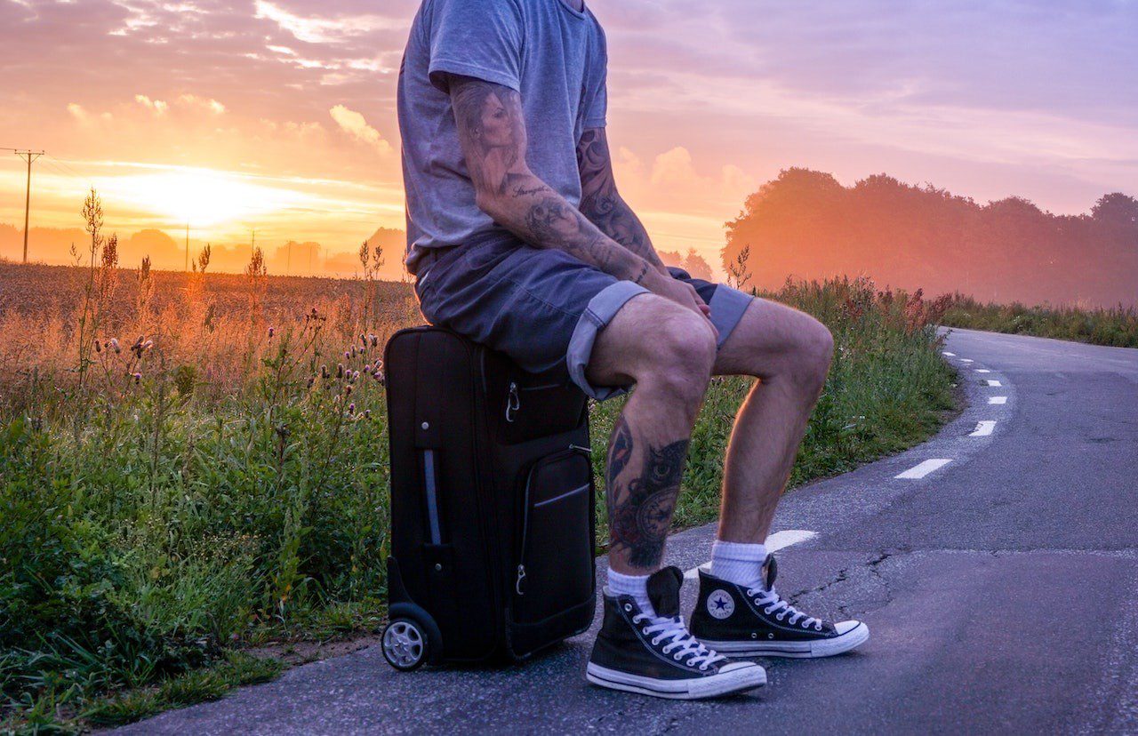 Image shows a man sat on suitcase - article provides info on how to avoid a holiday scam.