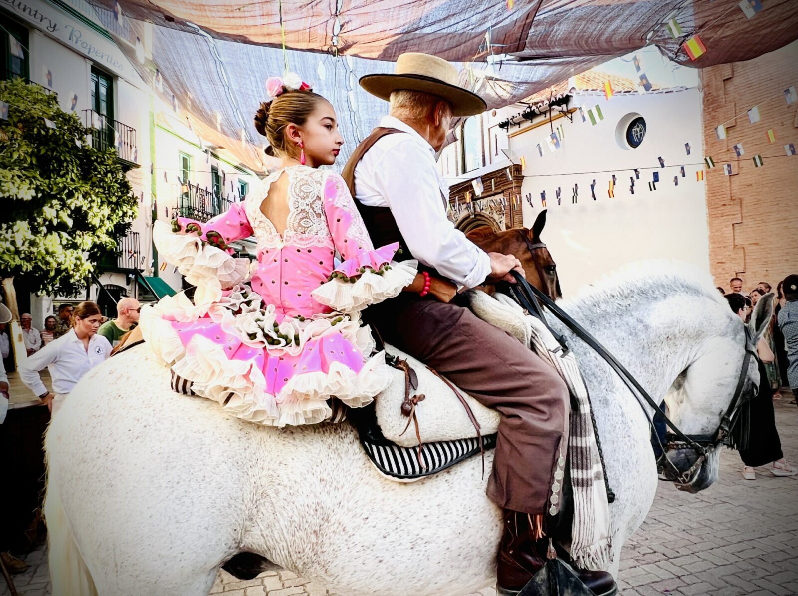 Image shows a grandfather with his daughter sat behind him on his horse as they participate in La Romería de San Sebastian at the Cómpeta Summer Feria.