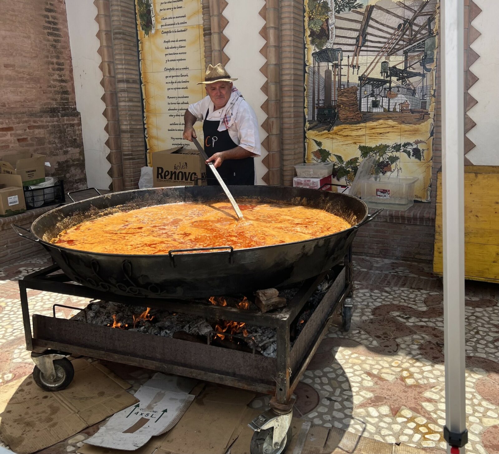 The image shows a local Competeño preparing a vast paella which will be given free to visitors at the Cómpeta Summer Feria